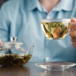 Kék inges férfi egyik kezével teáskannát fog, másikkal üvegcsészét zöld teával.