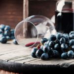 Kék szőlő és vörösbor egy üvegben és egy eldöntött talpas pohárban.
