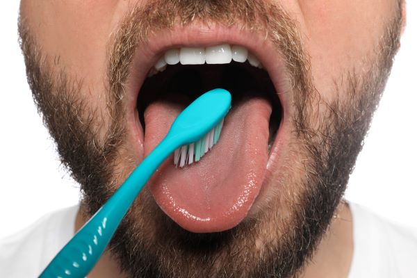Szakállas férfi kék fogkefével tisztítja a nyelvét.
