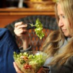 Hosszú hajú nő salátát eszik egy üvegtálból.