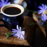 Kék csészében kávé, mellette cikóriavirág.