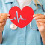 Kék köpenyes doktornő maga elé tart egy piros szívet, rajta EKG-jellel.