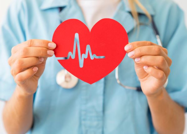 Kék köpenyes doktornő maga elé tart egy piros szívet, rajta EKG-jellel.