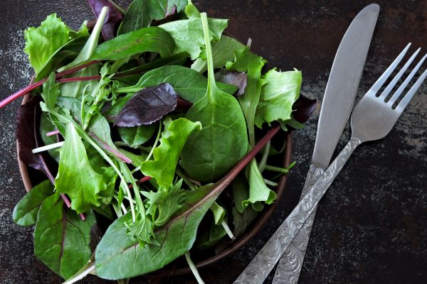 Egy tál zöld saláta, mellette kés és villa.