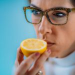 Szemüveges nő szagolgat egy fél citromot.