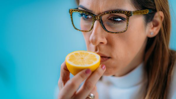 Szemüveges nő szagolgat egy fél citromot.