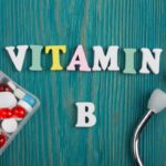 Kék deszkaháttéren színes "vitamin B" felirat, mellette gyógyszeradagolóban fehér, piros pirulák.