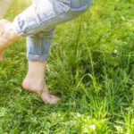 Miért jó mezítláb járkálni? Női lábak farmernadrágban mezítláb lépegetnek a fűben.