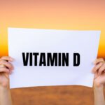 Az alacsony D-vitamin-szint következményei Női kezek egy fehér papírt tartanak fel a naplementés háttér előtt, "vitamin D" felirattal.
