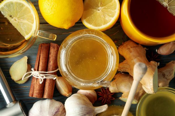 Faasztalon felülnézetben: üveg méz, csésze tea, citrom, köteg fahéjrúd, gyömbér, fokhagyma, csillagánizs.