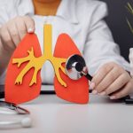 Fehér köpenyes doktornő egy tüdőmodellt tart a kezében, amelyet sztetoszkóppal vizsgál.