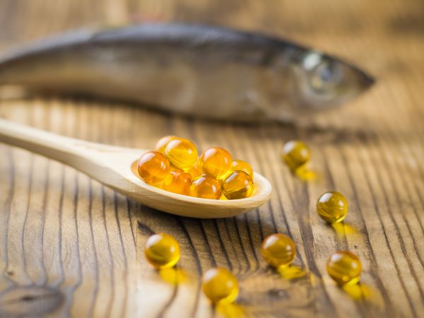 Fakanálban omega-3 kapszulák, a háttérben egy hal a faasztalon.