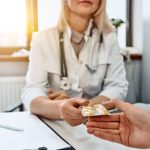 Doktornő a rendelőben az asztalnál ülve egy levélnyi kapszulát nyújt át a páciensnek.