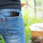 Farmernadrág farzsebéből kikandikáló mobiltelefon.
