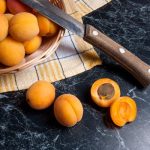 Márványos konyhapulton egy kosár sárgabarack és egy kés.