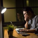 Férfi éjjel az íróasztalnál dolgozik ásítva a laptop előtt.