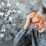 Gyógynövényekkel a memóriavesztés megelőzéséért Idős ősz hajú férfi a fejét fogja, a háttérben puzzle-darabok.