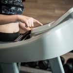 Nő beprogramoz egy edzőgépet, háttérben kézi súlyzók,