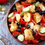 Felülnézetben lévő tányér paradicsommal, olajbogyókkal, cukkiniszeletekkel, pirítósdarabokkal, háttérben fokhagyma, villa.