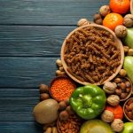 Faasztalon felülnézetben vegyes zöldségek, gyümölcsök, teljes kiőrlésű tészta, diófélék.