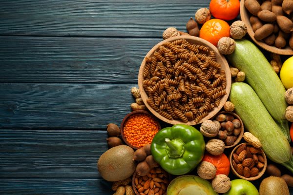 Faasztalon felülnézetben vegyes zöldségek, gyümölcsök, teljes kiőrlésű tészta, diófélék.