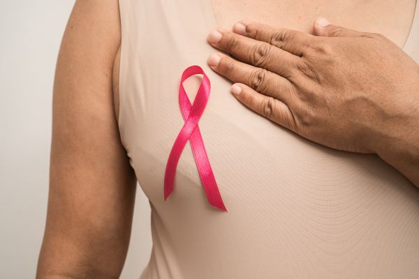 Nő egyik kezét a mellkasára teszi, ahol egy rózsaszínű szalag van a ruhájára tűzve.