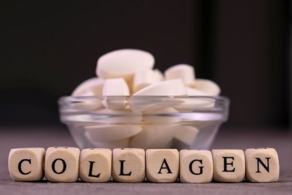 Fekete háttér előtt kis üvegtálban fehér ovális tabletták, előtte fakockákra írt betűkből összerakva a "collagen" szó.