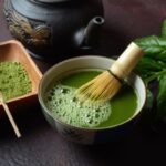 Kerámiatálban matcha tea, mellette fatálban matcha por, sötét teáskanna.