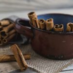 Régi kopott edényben fahéjrudak állnak, mellette a faasztalon is fahéjrudak.