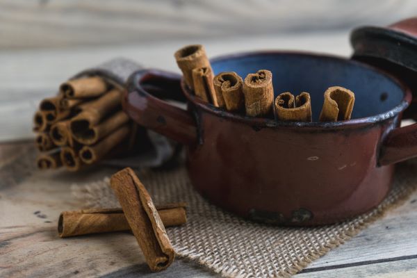 Régi kopott edényben fahéjrudak állnak, mellette a faasztalon is fahéjrudak.