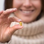 Fiatal nő két ujja között tart egy omega-3 kapszulát.