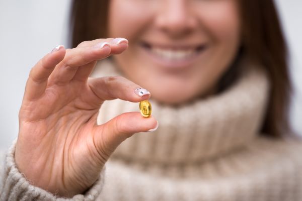 Fiatal nő két ujja között tart egy omega-3 kapszulát.