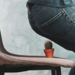 Férfi farmernadrágban leülni készül egy székre, amelyen egy kis cserép kaktusz van.l