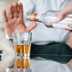 Üvegből valaki alkoholt tölt egy pohárba, míg egy kéz hárító mozdulatot tesz a pohár mögött.
