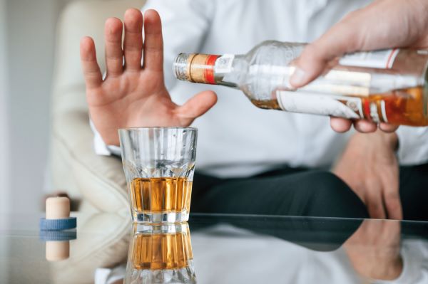 Üvegből valaki alkoholt tölt egy pohárba, míg egy kéz hárító mozdulatot tesz a pohár mögött.