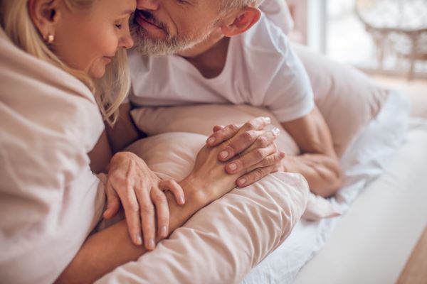 Idősebb pár az ágyban összebújva egymás kezét fogja.