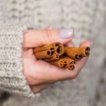 Közeli fotó egy köteg fahéjrúdról, amelyet egy nő tart a kezében.