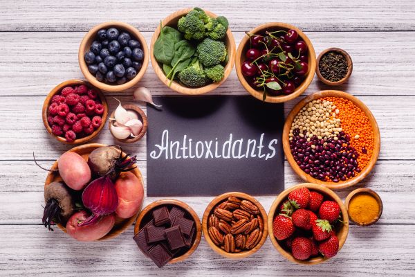 Felülnézetben fatálak különböző egészséges táplálékok, középen fekete tábla "antioxidants" felirattal.
