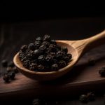 Sötét háttér előtt fakanálban feketebors-szemek.