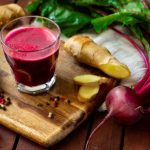 Vágódeszkán egy pohár céklalé, mellette gyömbér és színes bors, cékla.