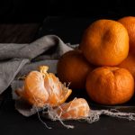 Sötét asztallapon egy kupac mandarin, amiből az egyik gyümölcs gerezdekre van szedve.