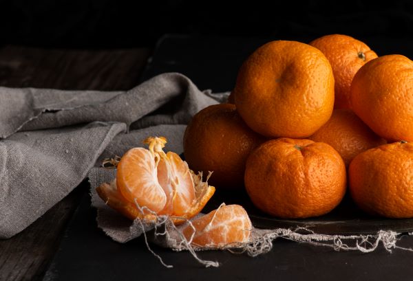 Sötét asztallapon egy kupac mandarin, amiből az egyik gyümölcs gerezdekre van szedve.