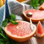 Ezek a táplálékok segítik a máj működését Grépfrút felszeletelve, kiskanál, kék-fehér csíkos konyharuhán, háttérben citrusfélék: citrom, lime.