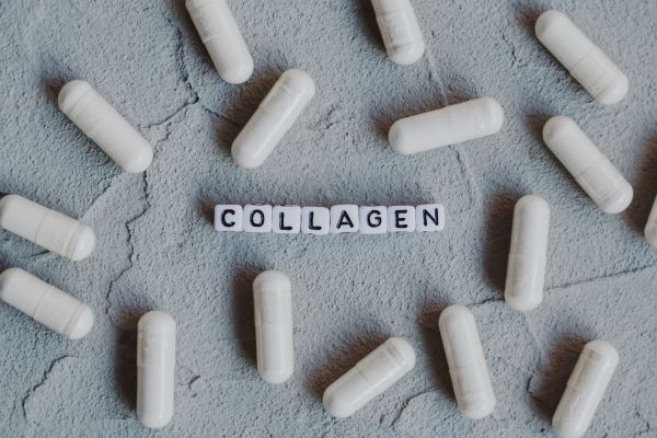 Repedt felületen fehér kapszulák, középen kis betűkockákból kirakva a "collagen" szó.