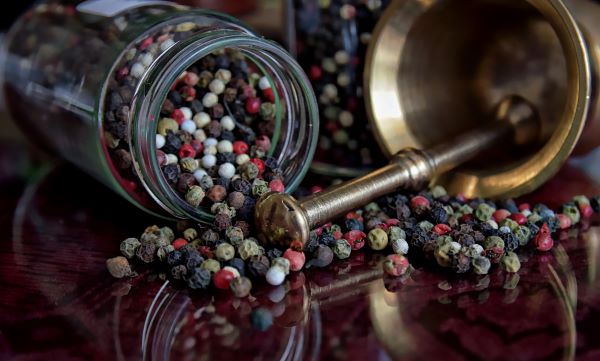 Egy üvegnyi színes bors eldöntve az asztalon, mellette rézmozsár szintén eldöntve, előttük az asztalon színesbors-szemek.