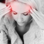 Milyen gyógynövények lehetnek a segítségünkre, ha fáj a fejünk? Fekete-fehér fotó nőről, aki mindkét kezével a halántékát fogja, a halántékán pirossal jelezve a fájdalom.