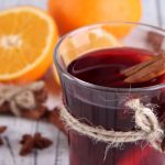 Egy pohár hibiszkusztea fahéjrudakkal, mellette narancs és csillagánizs.