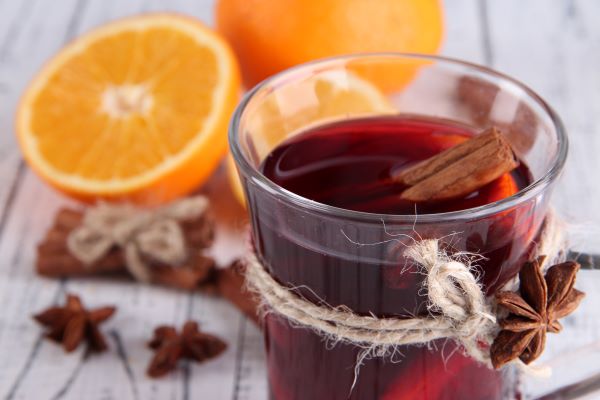 Egy pohár hibiszkusztea fahéjrudakkal, mellette narancs és csillagánizs.