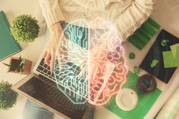Nő laptop előtt felülnézetben, előtte emberi agy hologramos ábrázolása.