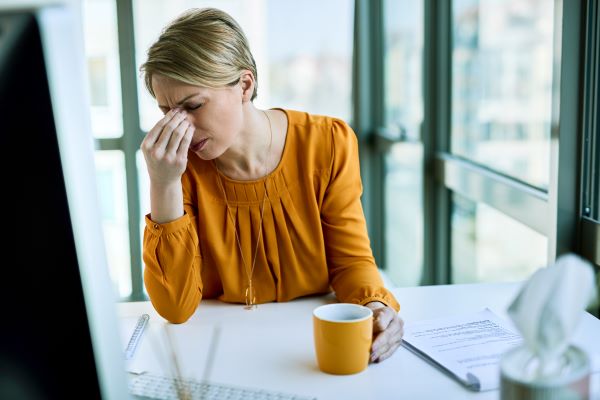 Nő mustársárga felsőben feszülten ül az íróasztalnál a monitor előtt, előtte egy sárga bögre és papírok.